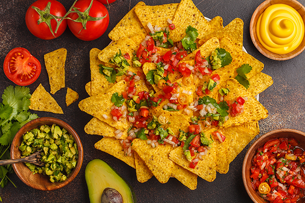 Mexican food concept. Nachos - yellow corn totopos chips with various sauces in wooden bowls: guacamole, cheese sauce, pico del gallo