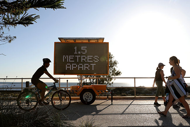 Members of the public are seen walking past a sign reading '1.5 Metres Apart' at Scarborough Beach, Perth, Monday, April 6, 2020. Beaches in Perth remain open but people must still adhere to social distancing rules. (AAP Image/Richard Wainwright) NO ARCHIVING