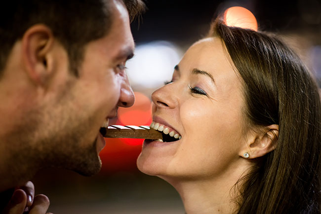 Young couple eating together one piece of chocolate - in street at night