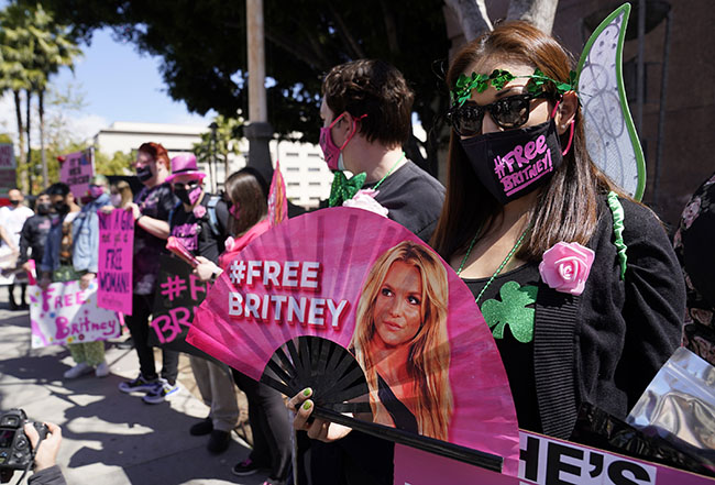 FILE - Britney Spears supporter Kiki Norberto holds a hand fan outside a court hearing concerning the pop singer's conservatorship on March 17, 2021, in Los Angeles. When Spears speaks to a judge at her own request on Wednesday, June. 23, 2021, she'll do it 13 years into a court-enforced conservatorship that has exercised vast control of her life and money by her father. Spears has said the conservatorship saved her from collapse and exploitation. But she has sought more control over how it operates, and says she wants her father out. (AP Photo/Chris Pizzello, File)