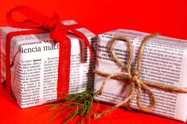 Alicante, Spain- November 11, 2021: Gifts wrapped in old newspaper with red bow and rope on red background