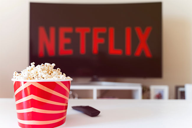 Istanbul, Turkey - July 03, 2020: Table with popcorn bottle and Netflix logo on TV. Netflix is a global provider of streaming movies and TV series.